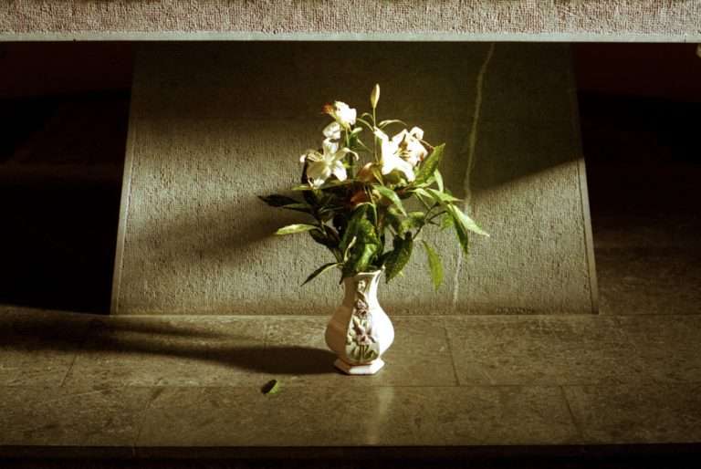 Un bouquet de lys blanc dans un vase en porcelaine orné d'iris, au pied d'un autel moderne dans l'église de La Mure en Isère, éclairage violent depuis la gauche et ombres portes fortes.